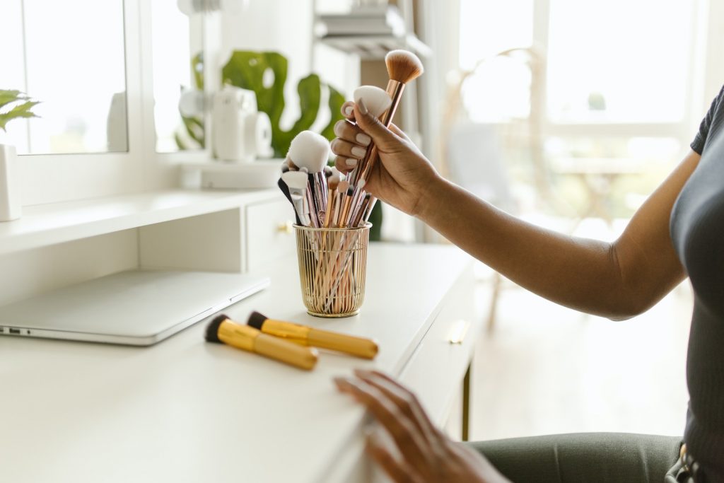 Person Holding Makeup Brushes From a Container